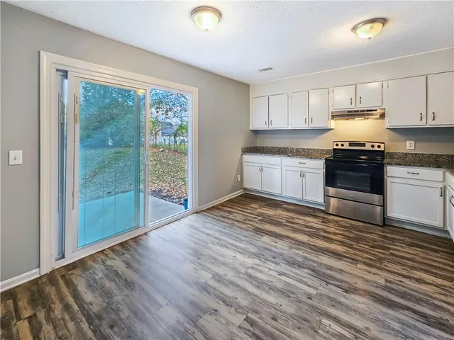 a kitchen with granite countertop wooden floors white cabinets and stainless steel appliances
