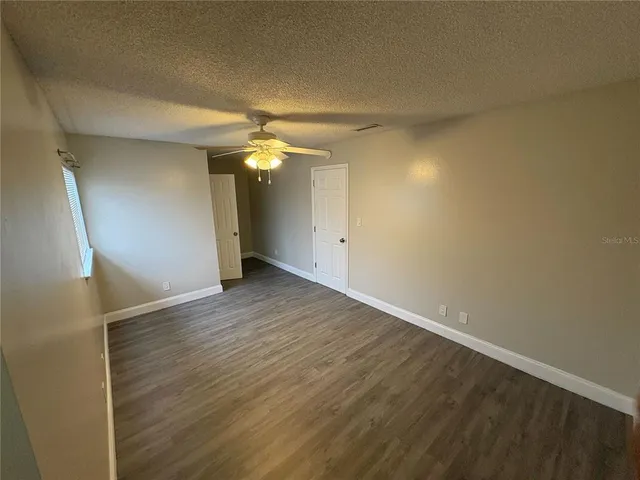 an empty room with wooden floor and way to kitchen