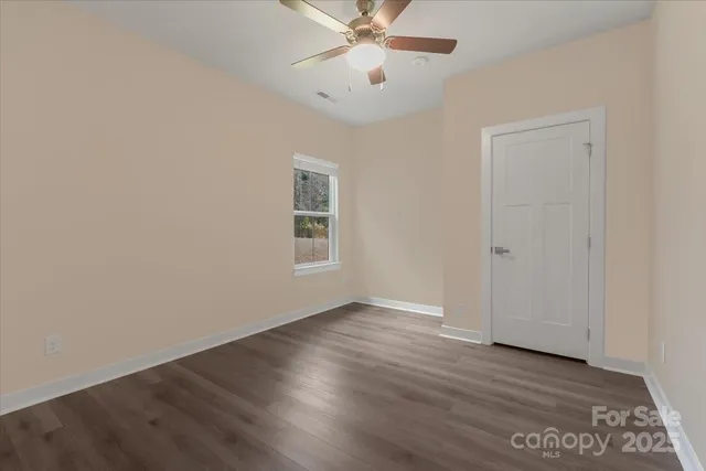 an empty room with wooden floor chandelier fan and windows