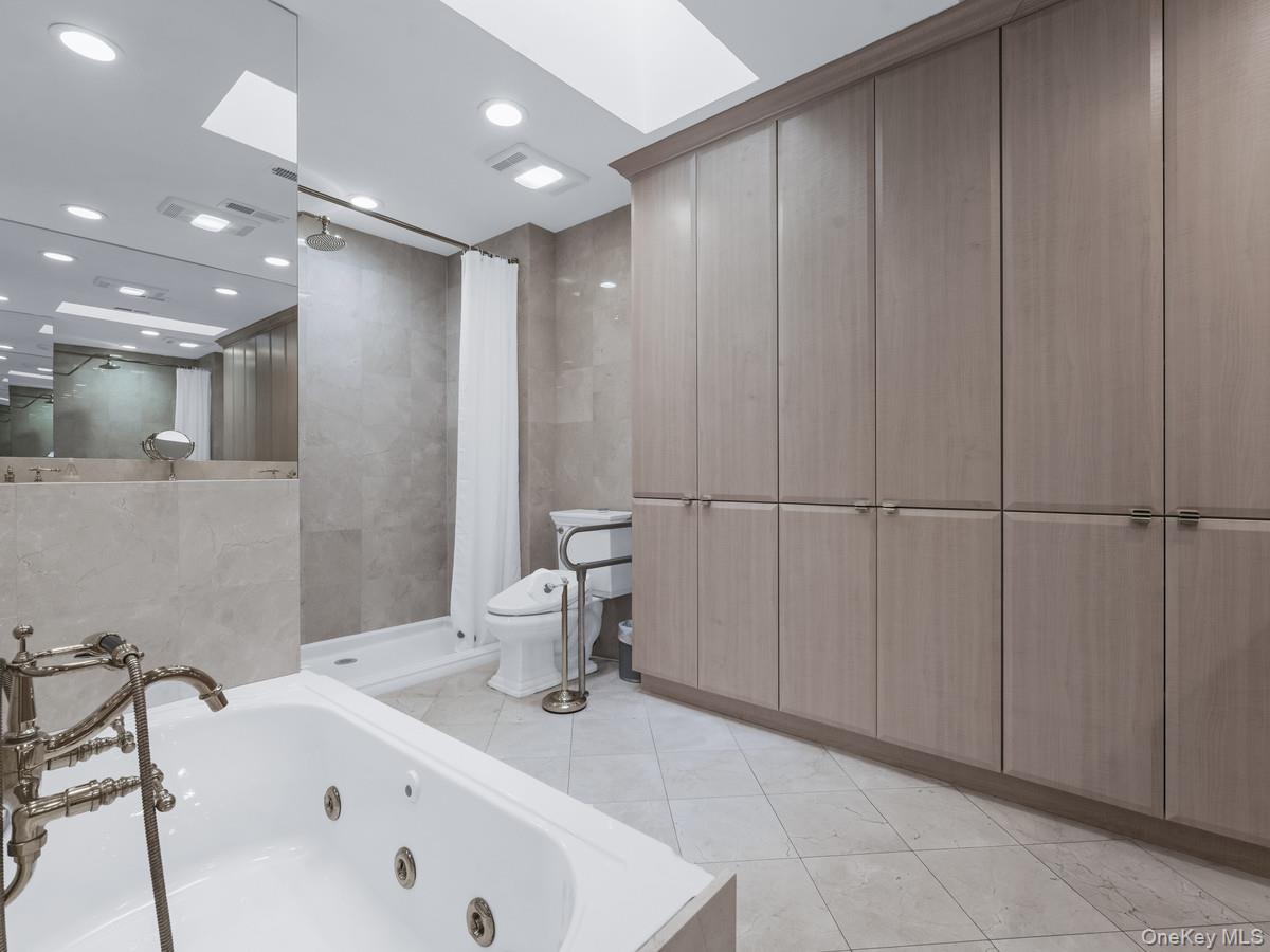 15 Fairway Circle South, Unit 15 Manhasset, NY 11030 - Photo 22 of 39 First Floor Primary Bathroom with light tile patterned flooring, a whirlpool tub, a stall shower, a skylight, and tile walls