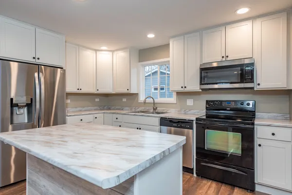 a kitchen with kitchen island granite countertop a stove top oven a sink a counter space and cabinets