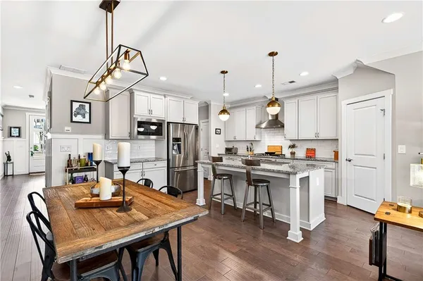 a kitchen with stainless steel appliances kitchen island granite countertop a table chairs refrigerator and microwave