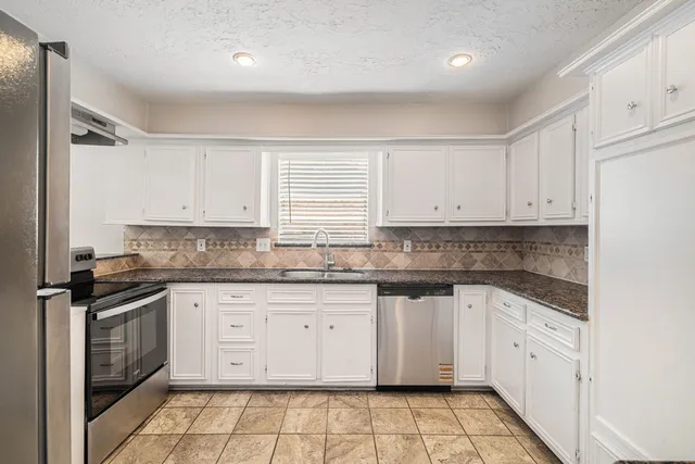 a kitchen with granite countertop white cabinets stainless steel appliances a sink and a window