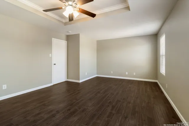 a view of an empty room with wooden floor and a ceiling fan