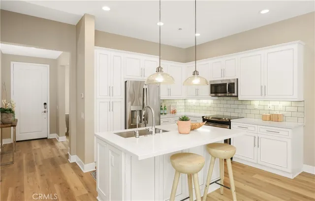 a kitchen with granite countertop a sink a stove a refrigerator and white cabinets with wooden floor