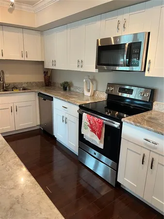 a kitchen with granite countertop a stove top oven a sink dishwasher and white cabinets with wooden floor