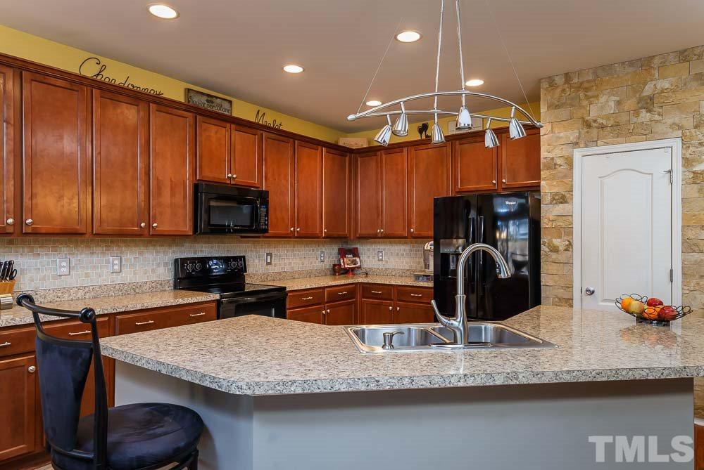 131 Daneborg Road Durham, NC 27703 - Photo 8 of 25 Rich wood cabinets galore, tile backsplash, stone accent wall, and a pantry. Texture and beauty perfectly blended with high function!