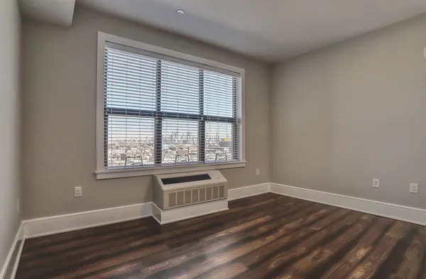 a view of an empty room with wooden floor and a window