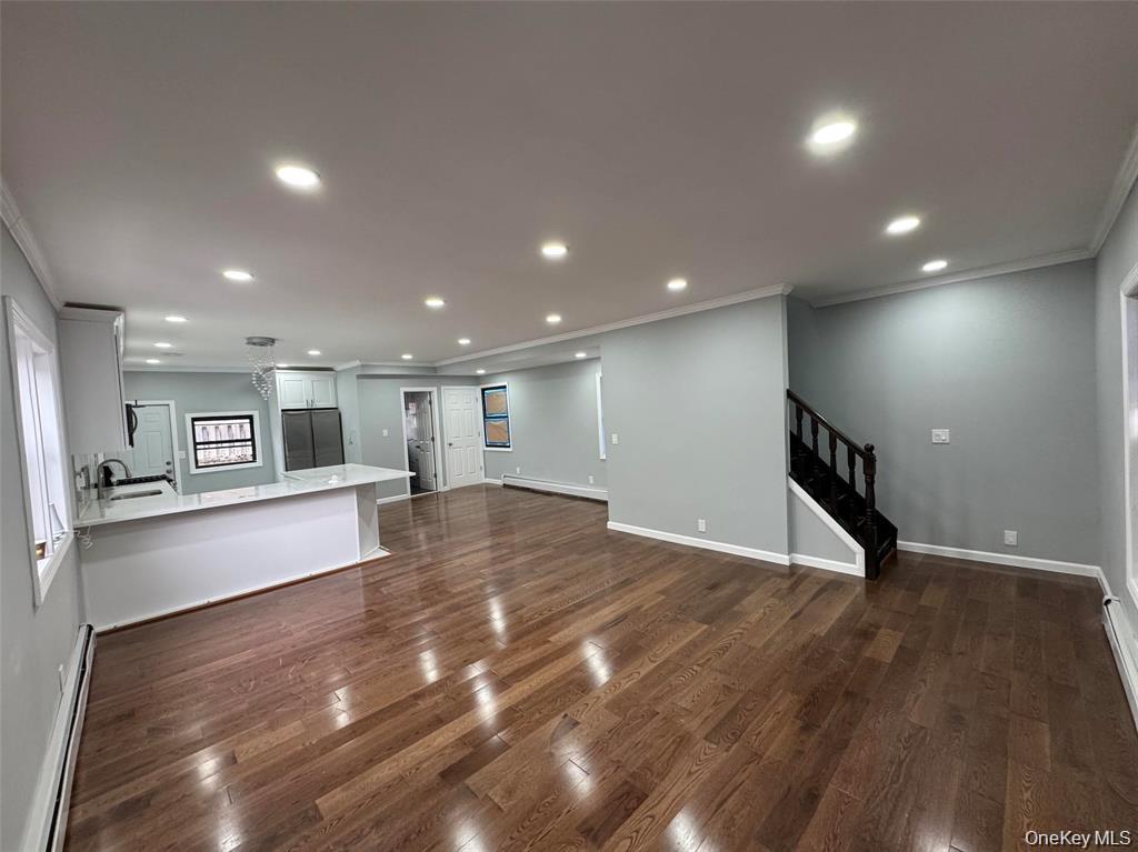 Unfurnished living room with ornamental molding, stairs, baseboard heating, dark wood-style floors, and recessed lighting