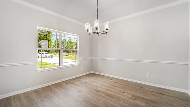 an empty room with wooden floor chandelier and windows