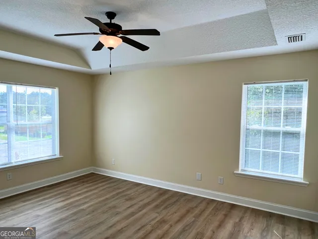 an empty room with wooden floor ceiling fan and windows