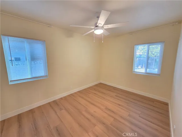 a view of an empty room with wooden floor and a ceiling fan