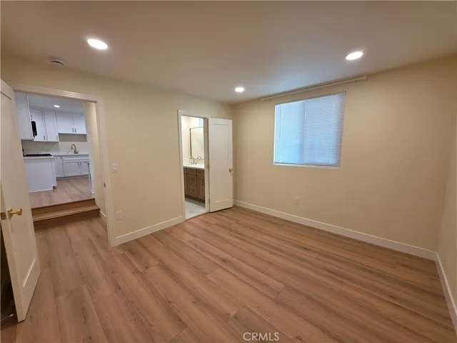 a view of an empty room with wooden floor and a kitchen