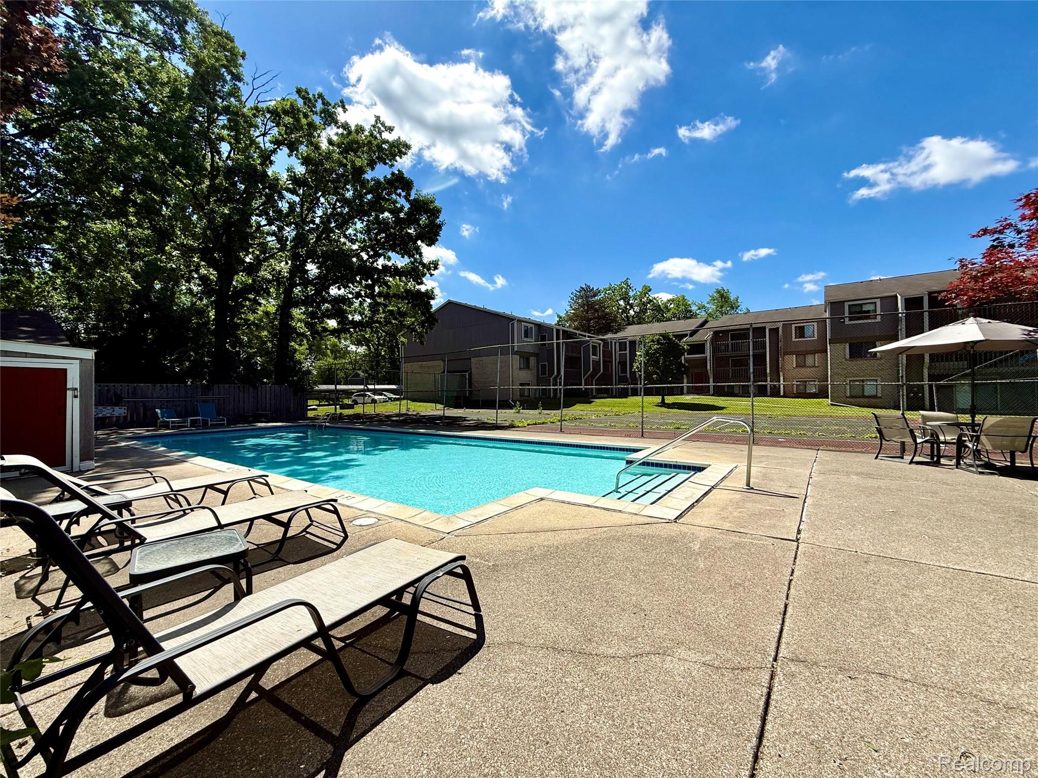 29870 West 12 Mile Road, Unit 703 Farmington, MI 48334 - Photo 36 of 40 Outdoor swimming pool with concrete surround, featuring steps with handrails, and mature trees providing natural shading