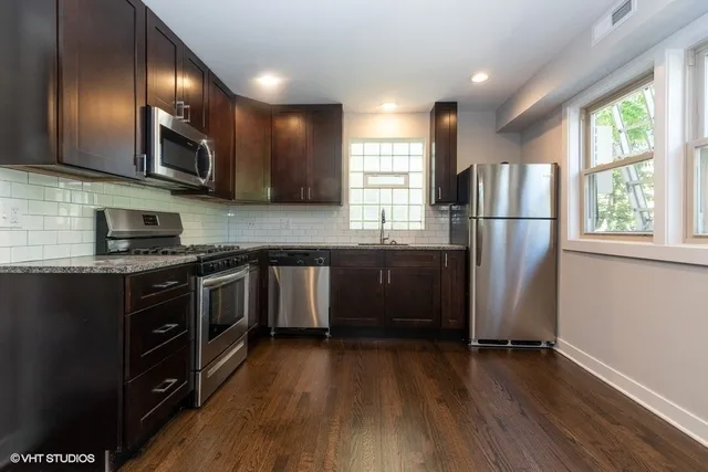 a kitchen with stainless steel appliances granite countertop wooden cabinets a refrigerator a sink a stove a microwave and wooden floors