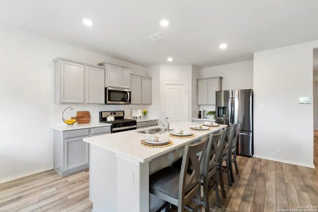 a kitchen with a refrigerator a stove a microwave oven a sink and a dining table with wooden floor