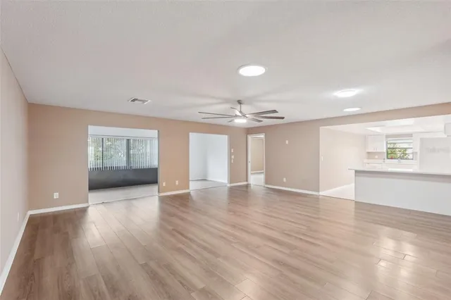 a view of an empty room with wooden floor and a ceiling fan