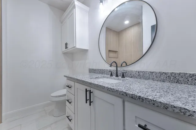 a bathroom with a granite countertop toilet a sink and a mirror