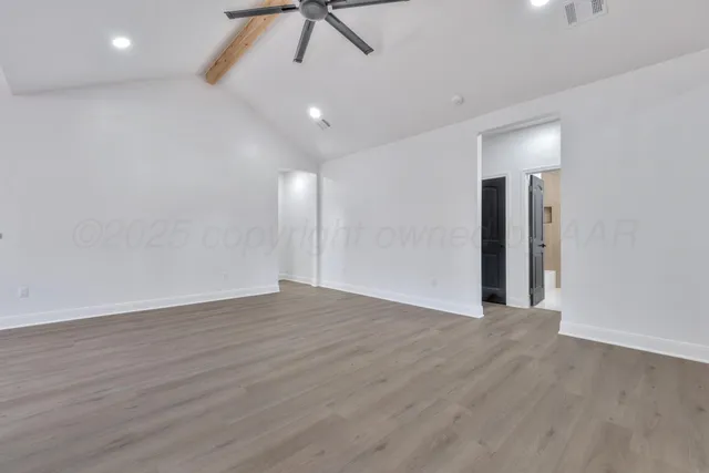 a view of an empty room with wooden floor and a ceiling fan
