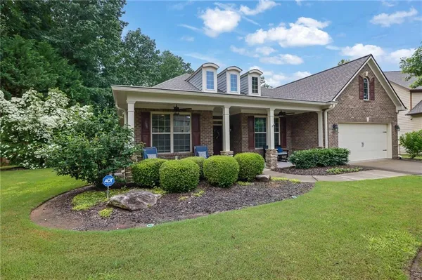 a view of a brick house with a yard plants and large tree