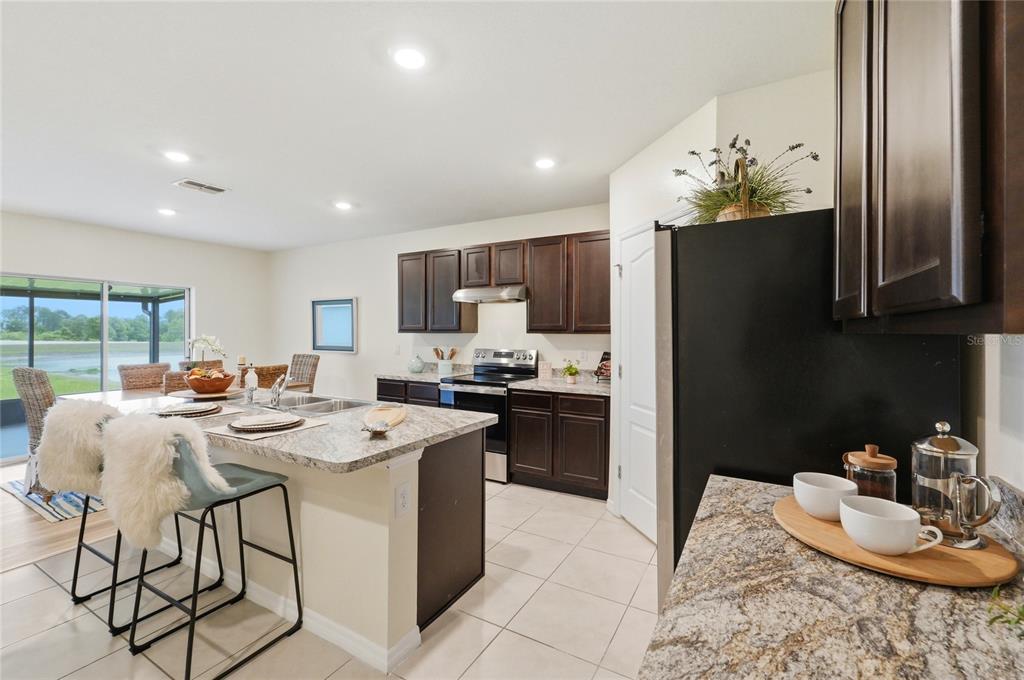 416 Corso Loop Winter Haven, FL 33884 - Photo 17 of 73 a kitchen with stainless steel appliances granite countertop a stove a refrigerator a sink a dining table and chairs with wooden floor
