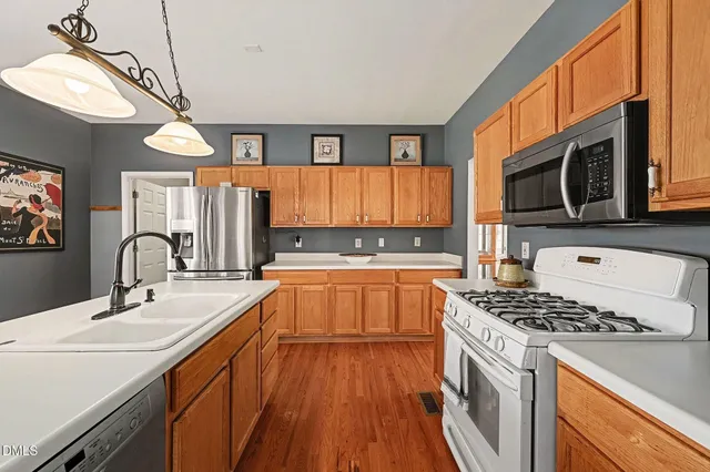 a kitchen with stainless steel appliances a sink dishwasher stove refrigerator and microwave with wooden floor