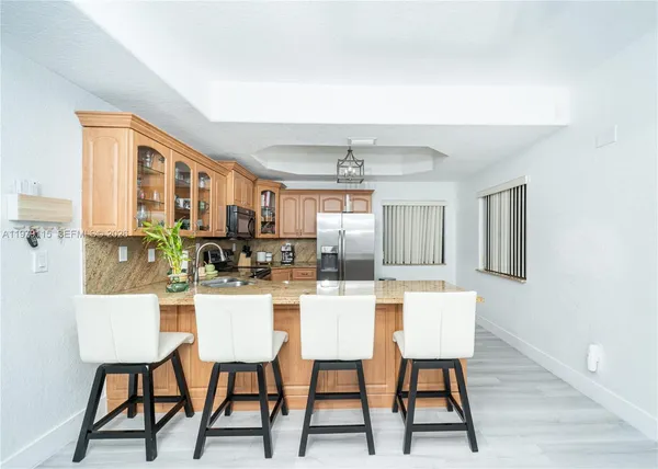 a kitchen with stainless steel appliances kitchen island granite countertop a dining table chairs and a refrigerator