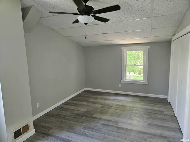 an empty room with wooden floor fan and windows