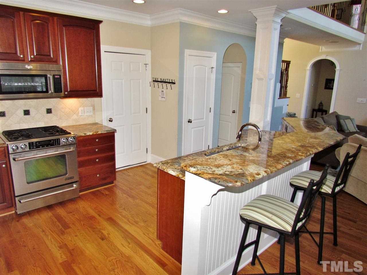 3810 Congeniality Way Raleigh, NC 27613 - Photo 10 of 25 View of kitchen looking from eat-in area. Note upgraded gas range and cabinets and granite bar. Hardwoods are on almost all of the first floor. Door on right leads to 2 car side load garage.Convenient to move groceries/stuff/kids to house.