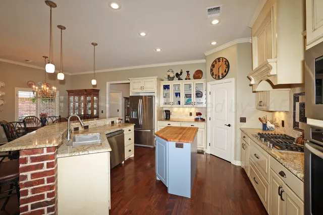 a kitchen with stainless steel appliances kitchen island granite countertop a stove a sink a refrigerator and white cabinets with wooden floor