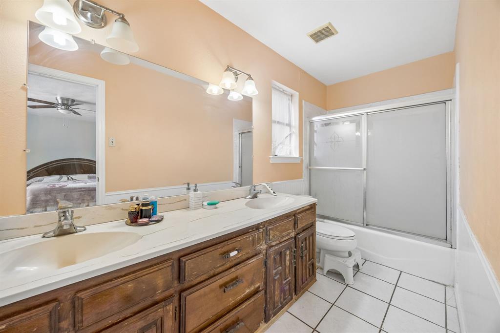 1701 East Spring Valley Road Richardson, TX 75081 - Photo 19 of 28 Dual vanity with white countertop, full-width mirror, white tile flooring, and a shower/tub combination with sliding frosted glass doors