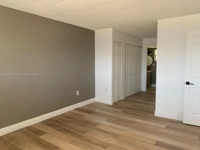 a view of an empty room with wooden floor and closet