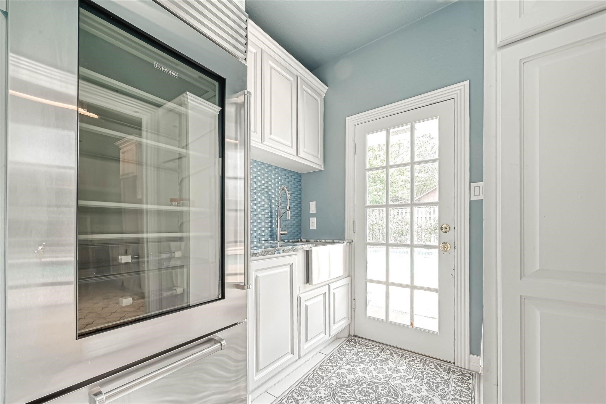 263 Wood Loop Street Houston, TX 77015 - Photo 38 of 45 This kitchen nook features sleek stainless steel appliances, white cabinetry, a stylish blue tile backsplash, and a patterned floor. A glass-paneled door offers ample natural light and outdoor access.