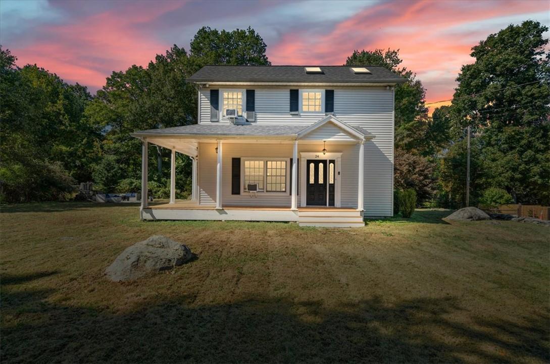 Back house at dusk with a lawn and covered porch
