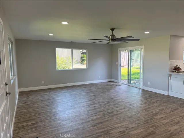 an empty room with wooden floor ceiling fan and windows