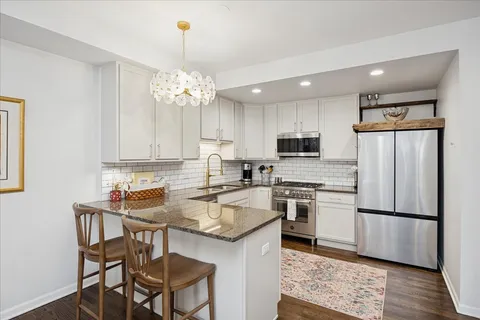 a kitchen with stainless steel appliances granite countertop a stove top oven a refrigerator a sink and a dining table with wooden floor