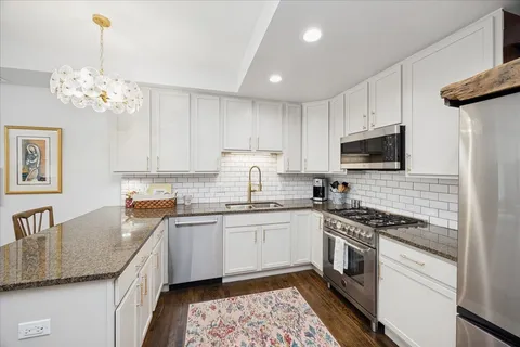 a kitchen with stainless steel appliances granite countertop a sink a stove top oven a refrigerator with white cabinets and wooden floor