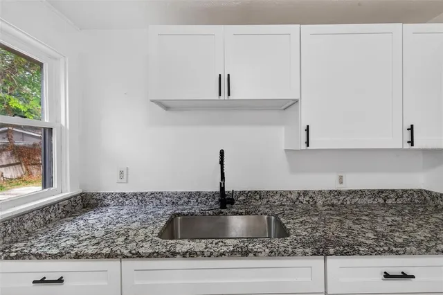 a kitchen with granite countertop a sink and white cabinets