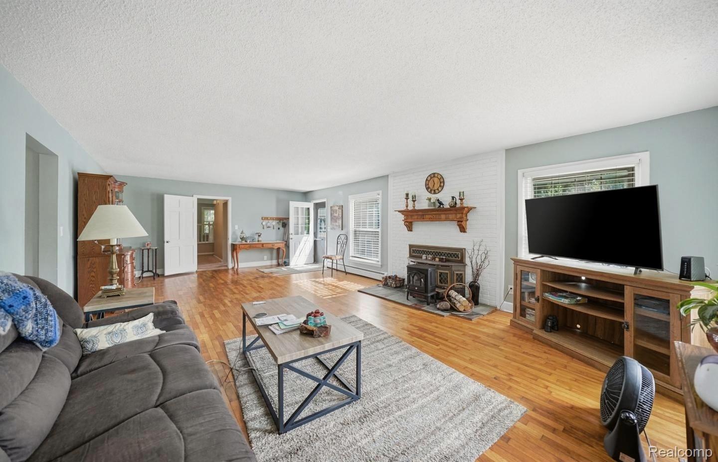 6790 Weyer Road Imlay City, MI 48444 - Photo 6 of 34 Spacious living area featuring wood-finish flooring, a white brick fireplace with a wood mantle, and a wood stove insert
