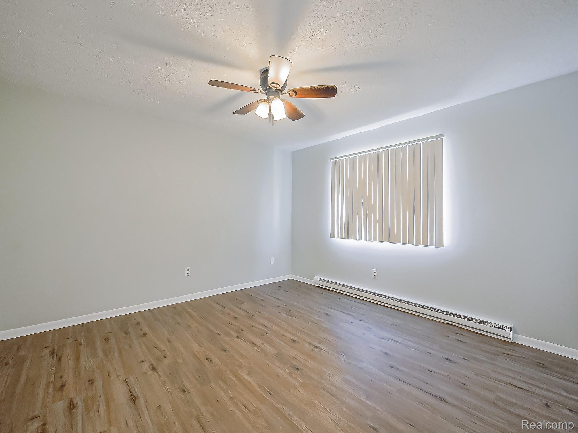 125 East Van Riper Road, Unit 7 Fowlerville, MI 48836 - Photo 11 of 26 Spare room with baseboard heating, light wood finished floors, ceiling fan, and a textured ceiling