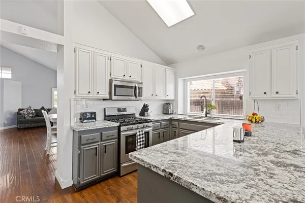 a kitchen with stainless steel appliances granite countertop a stove top oven a sink a dining table and chairs with wooden floor