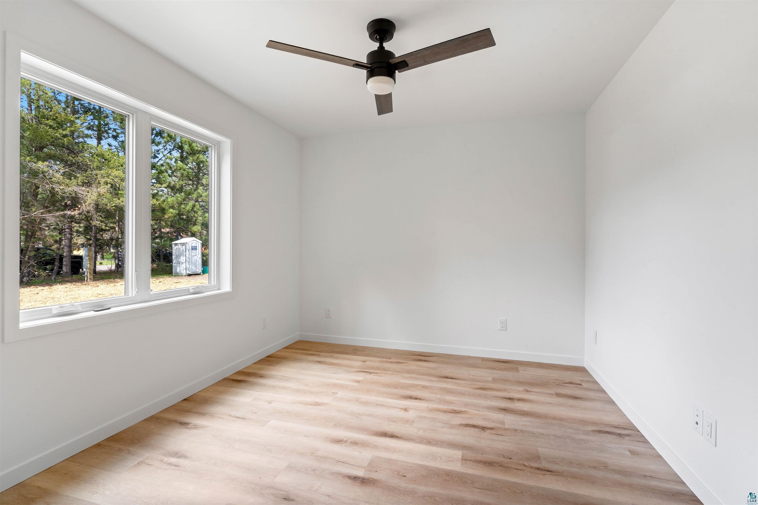 1386 Stephen Road Cloquet, MN 55720 - Photo 20 of 25 Bright room featuring a large double window, wood-finish flooring, white walls, and a ceiling fan with integrated lighting
