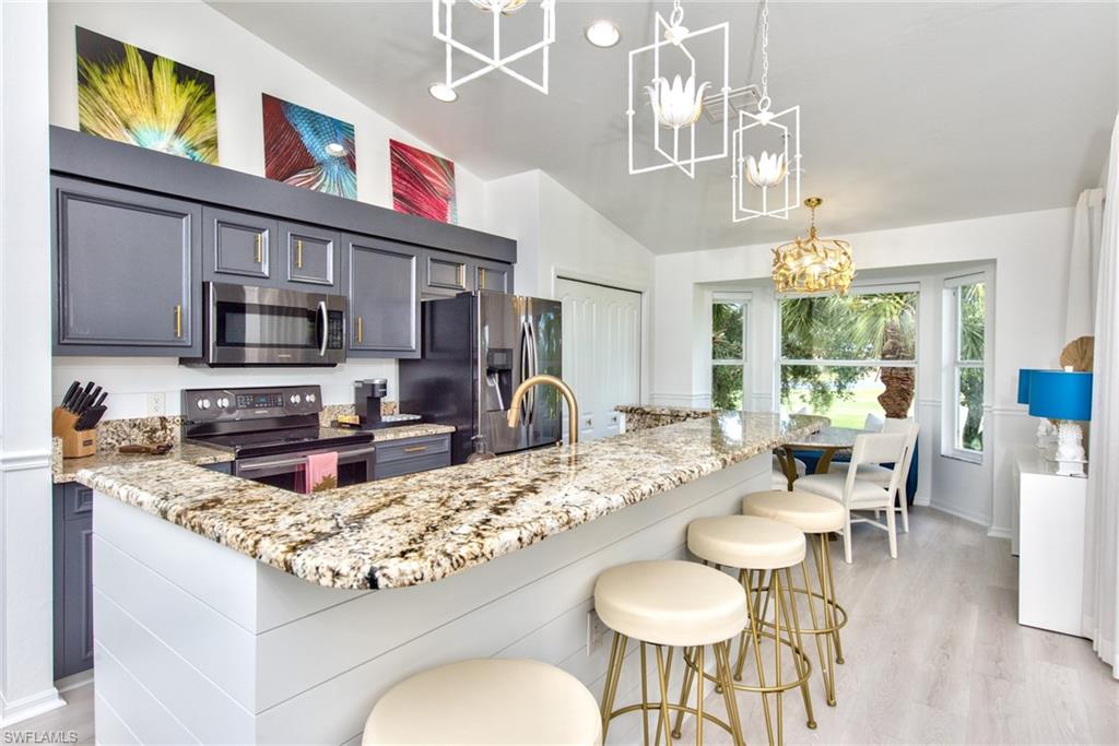 21340 Lancaster Run, Unit 1327 Estero, FL 33928 - Photo 5 of 27 a kitchen with stainless steel appliances granite countertop a stove a sink dishwasher a dining table and chairs with wooden floor