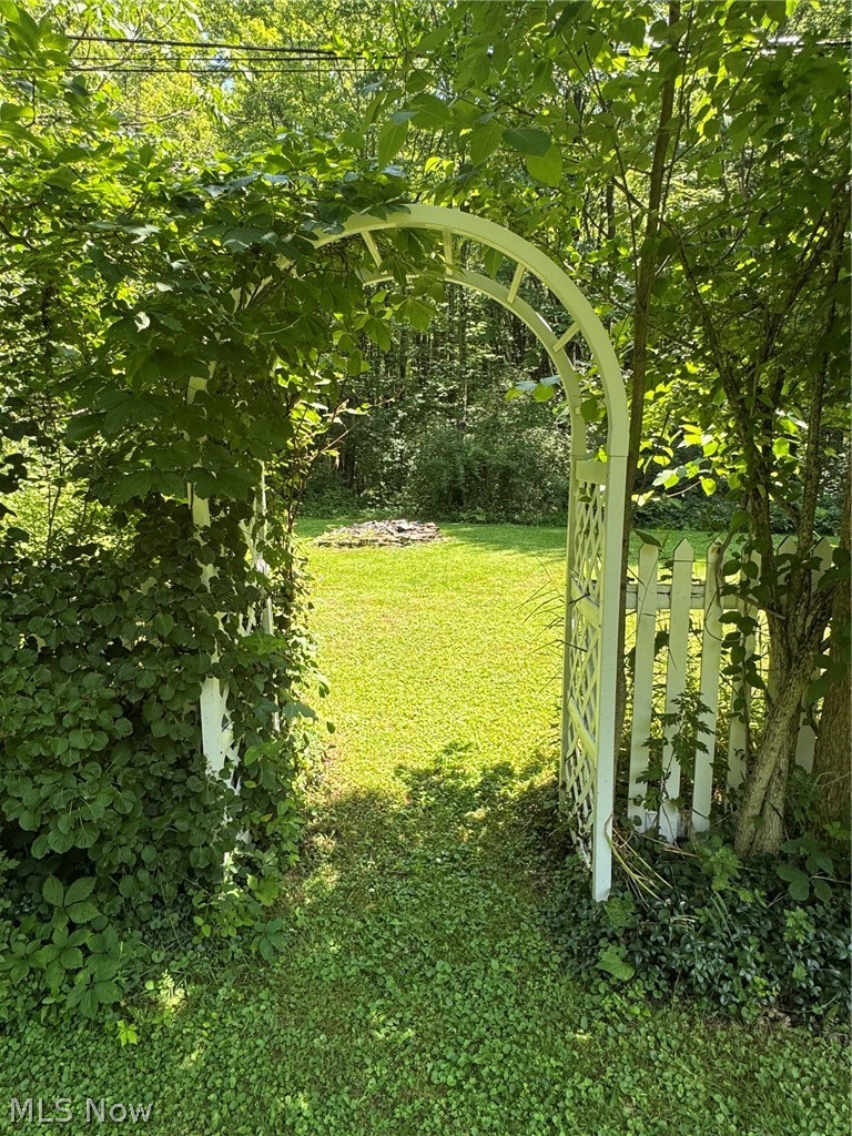 8201 Orchard Road Painesville, OH 44077 - Photo 42 of 45 Garden entry with a white archway and picket fence, opening to a sunlit lawn