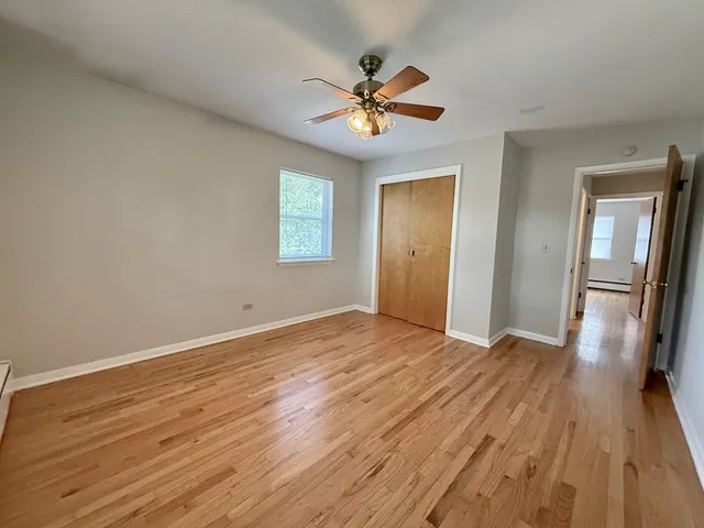 a view of an empty room with wooden floor and a ceiling fan