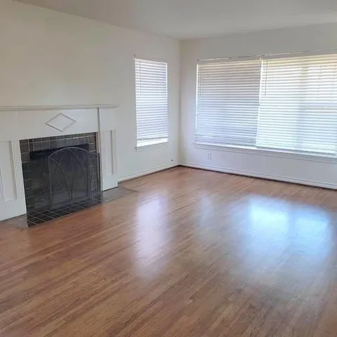 an empty room with wooden floor fireplace and windows