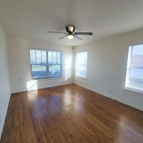 an empty room with wooden floor chandelier fan and windows