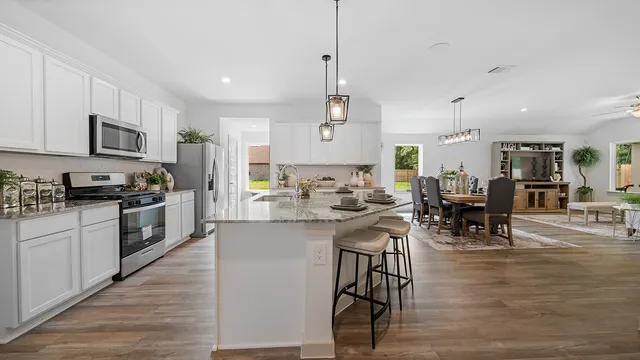 a kitchen with stainless steel appliances granite countertop a stove top oven a sink a dining table and chairs with wooden floor