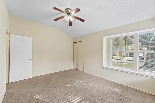 an empty room with chandelier fan and windows