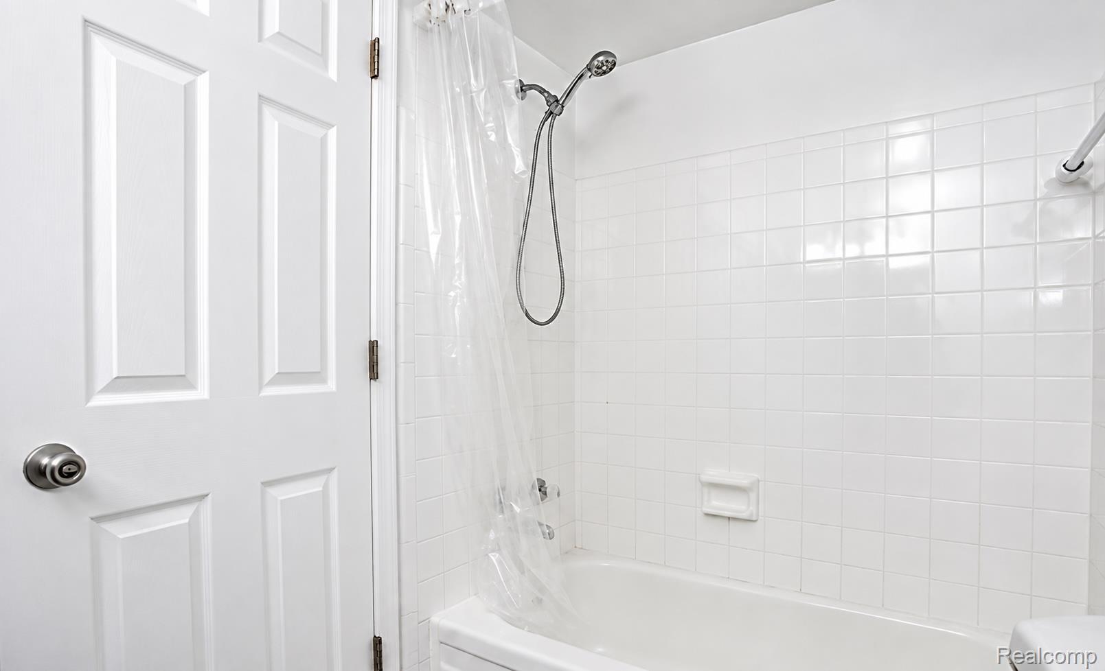 White paneled door with brushed nickel hardware, white subway tile surround, and a chrome shower head